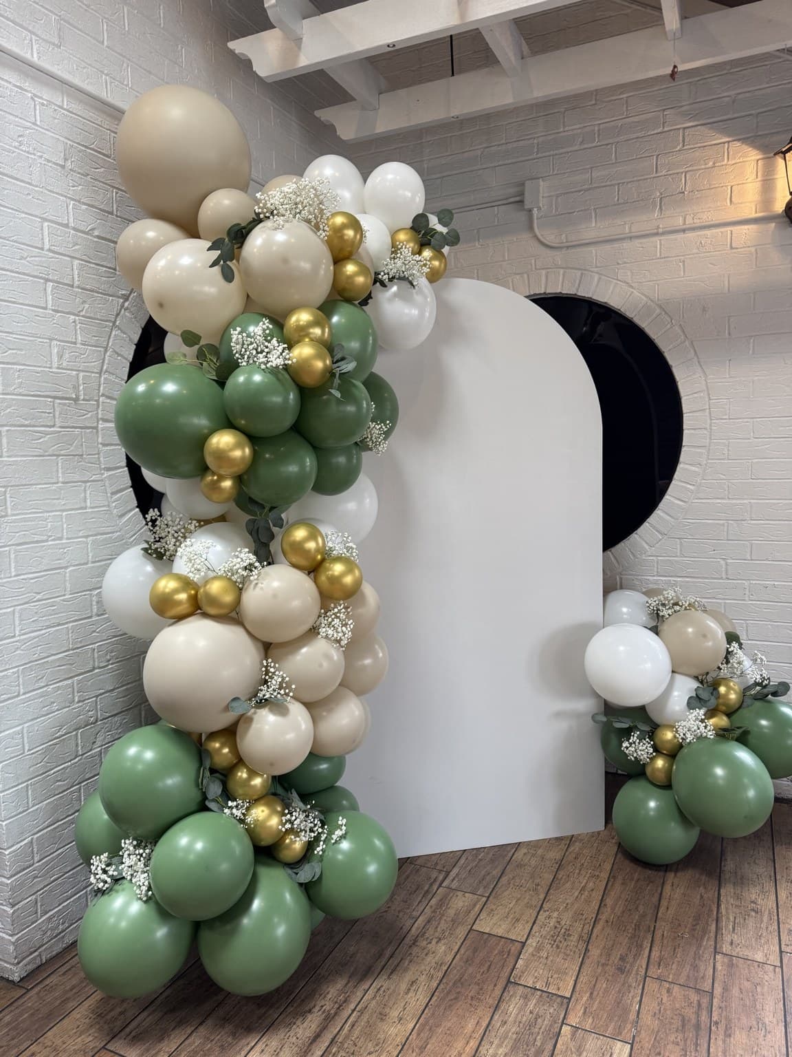 Sage, cream, and gold balloon garland with flowers around a white backdrop