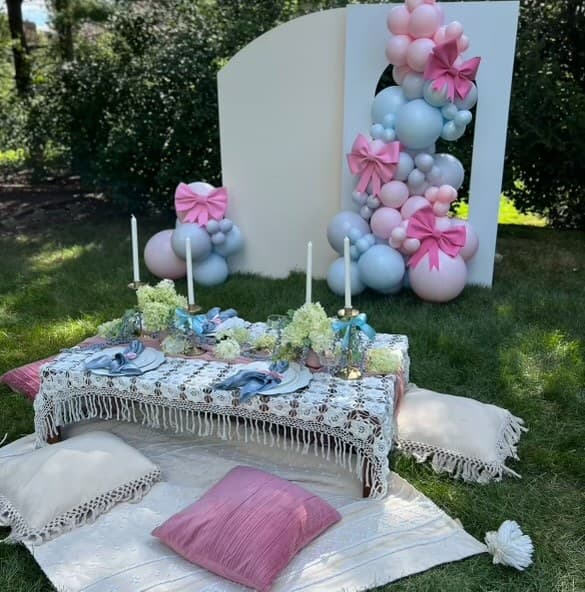 Pastel balloon backdrop with a low table and cushions for an outdoor celebration